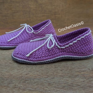 May include: A pair of purple crocheted slippers with white trim and laces. The slippers have a textured knit pattern and are made with a soft yarn.