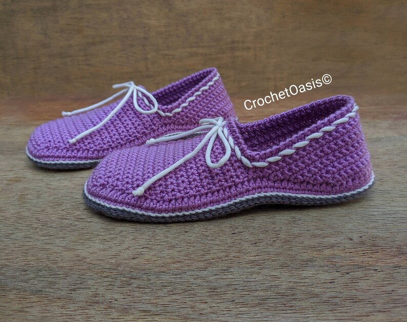 May include: A pair of purple crocheted slippers with white trim and laces. The slippers have a textured knit pattern and are made with a soft yarn.