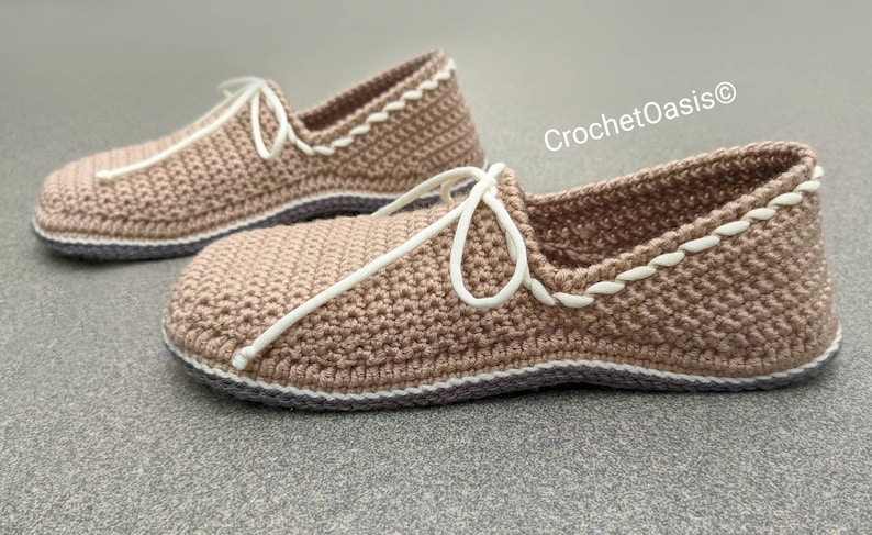 May include: A pair of crocheted slippers in a light brown color with white trim. The slippers have a simple design and are tied with white laces.