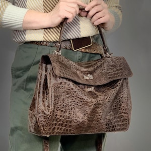 May include: A brown leather handbag with a crocodile pattern and a long strap. The bag has a top flap with a silver clasp.