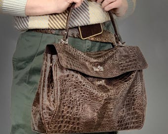 May include: A brown leather handbag with a crocodile pattern and a long strap. The bag has a top flap with a silver clasp.