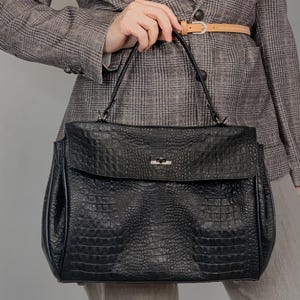 May include: A black leather handbag with a crocodile-embossed texture and a silver clasp. The bag has two top handles and a structured shape.