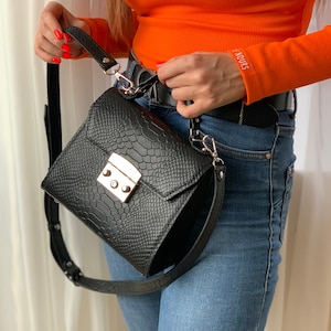 May include: A black leather handbag with a snakeskin pattern and a gold clasp. The bag has a long adjustable strap and a top handle.