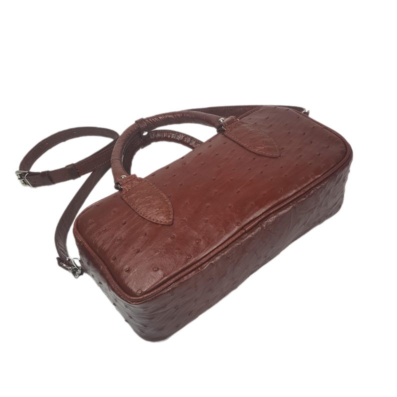 May include: A brown leather handbag with a textured surface, featuring a top handle and a detachable shoulder strap. The bag has a rectangular shape and silver-colored hardware.