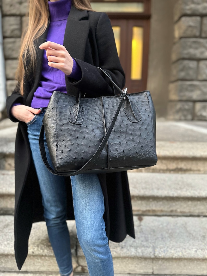 May include: A black leather tote bag with a textured ostrich pattern. The bag has a top handle and a long shoulder strap.