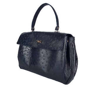 May include: A navy blue handbag with a textured surface and a top handle. The bag features a flap closure with a gold-colored clasp. The handbag has a structured design and a classic, elegant style.