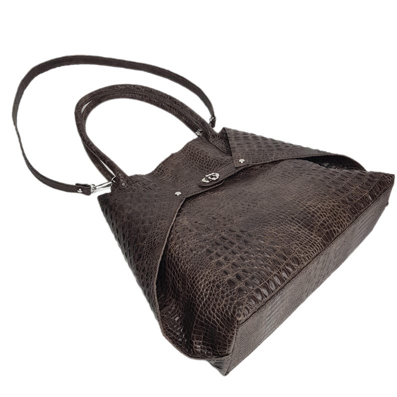 May include: A brown leather tote bag with a crocodile embossed pattern and a silver buckle closure.