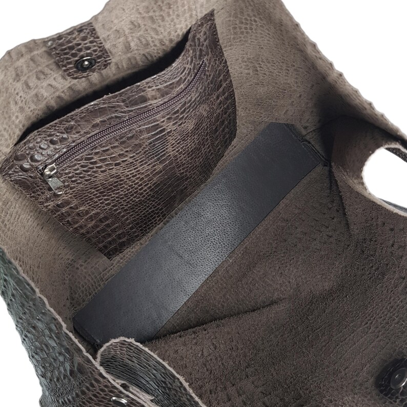 May include: A brown leather tote bag with a zippered pocket and a flap closure. The bag is lined with a dark fabric and has a textured exterior.