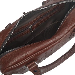 May include: A brown leather briefcase with an open zipper revealing the interior pockets. The bag has a textured surface and a handle on the side. The zipper is silver and the interior is a darker brown.