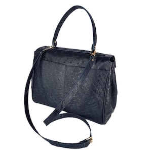 May include: A navy blue handbag with a textured surface, featuring a top handle and a detachable shoulder strap. The bag has gold-colored hardware and a flap closure. The design includes a front pocket and a structured silhouette.