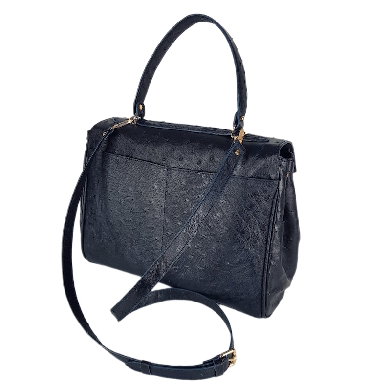 May include: A navy blue handbag with a textured surface, featuring a top handle and a detachable shoulder strap. The bag has gold-colored hardware and a flap closure. The design includes a front pocket and a structured silhouette.
