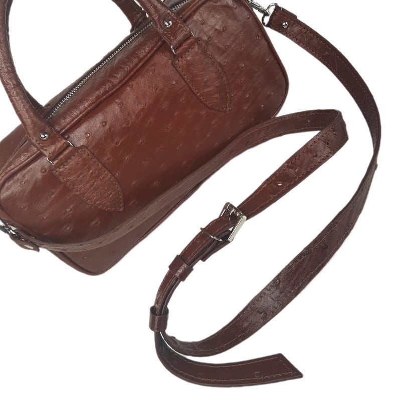 May include: A brown leather handbag with a textured surface and a silver zipper. The bag has a matching adjustable shoulder strap and a top handle. The bag is approximately 10 inches long.