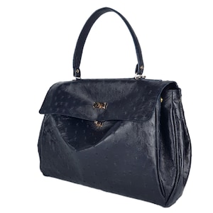 May include: A navy blue handbag with a textured surface and a top handle. The bag features a flap closure with a gold-colored clasp. The bag has a structured design and a rounded shape.
