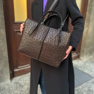 May include: A brown leather tote bag with a textured ostrich pattern. The bag has two top handles and a long shoulder strap.