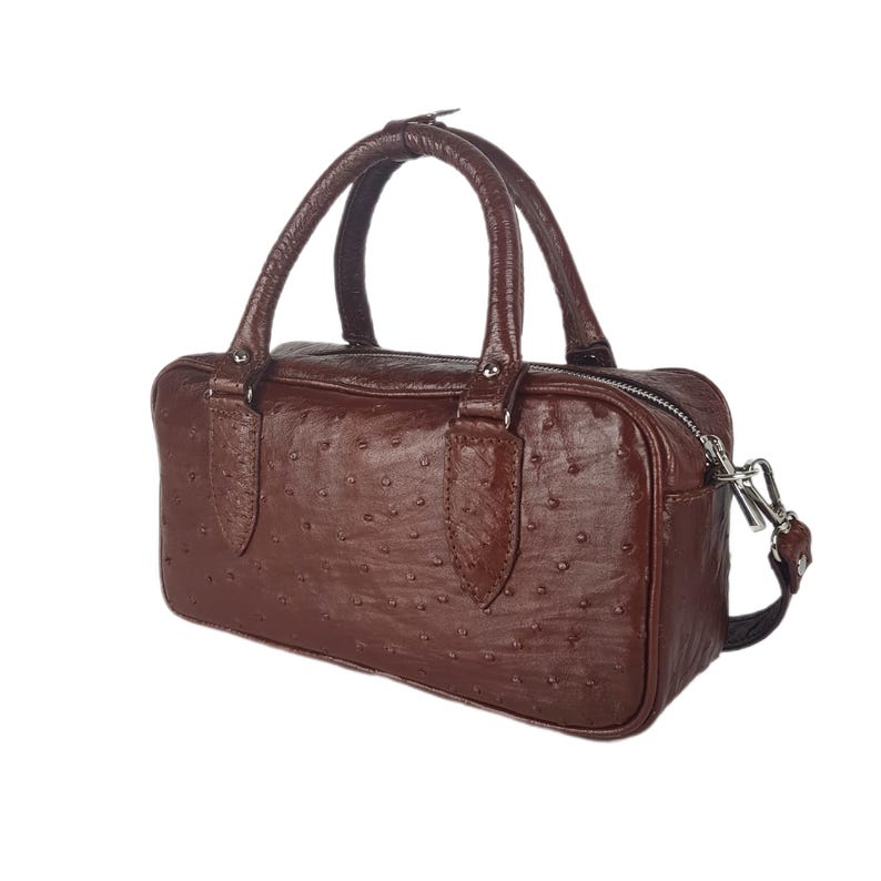 May include: A brown leather handbag with a textured ostrich pattern. The bag has two top handles and a silver zipper closure. It also includes a detachable shoulder strap. The bag is rectangular and has a classic design.