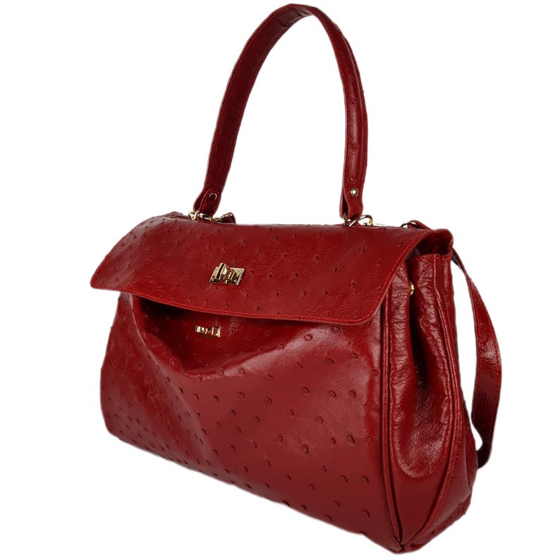 May include: A red handbag with a textured surface and a flap closure. The bag has a top handle and a detachable shoulder strap. The hardware is gold-toned. The bag has a small logo on the front.