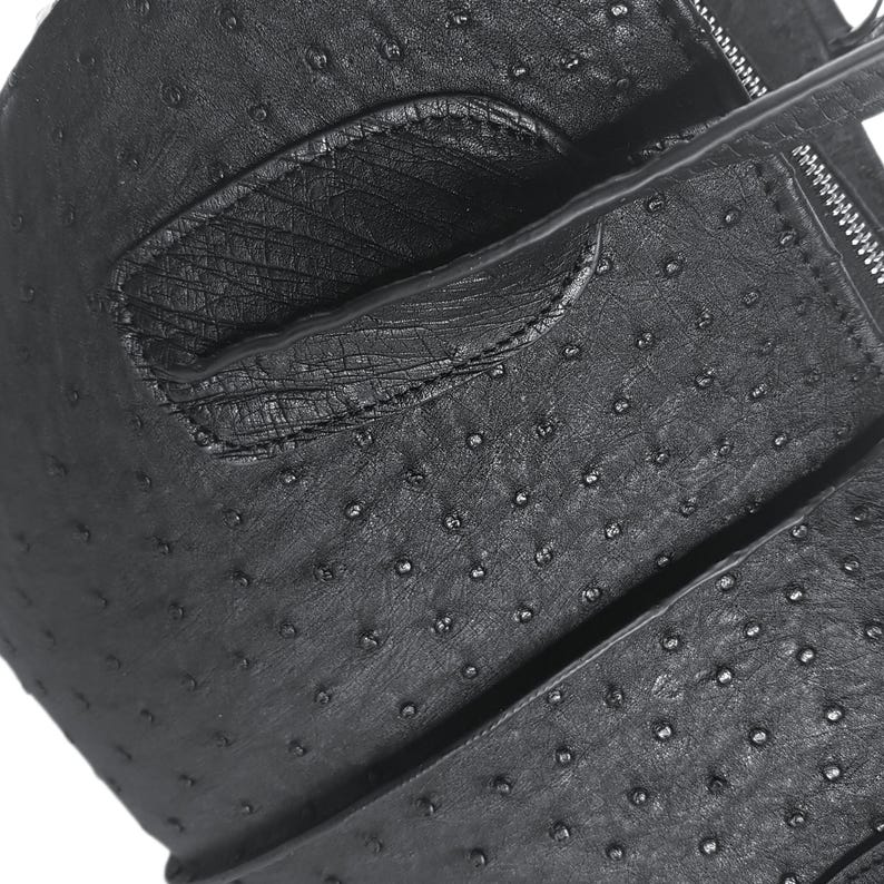 May include: Black leather bag with a textured ostrich-like pattern. The bag has a flap closure and a zipper detail.