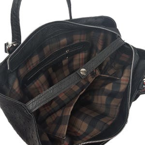 May include: Black leather tote bag with a plaid lining and a zipper closure. The bag has a top handle and a shoulder strap.