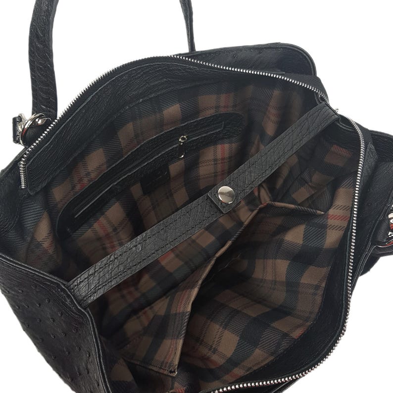 May include: Black leather tote bag with a plaid lining and a zipper closure. The bag has a top handle and a shoulder strap.
