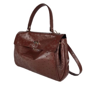 May include: A brown leather handbag with a top handle and a shoulder strap. The bag has a flap closure with a gold-colored clasp. The leather has a textured, dotted pattern.