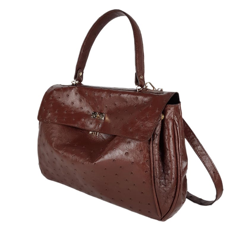 May include: A brown leather handbag with a top handle and a shoulder strap. The bag has a flap closure with a gold-colored clasp. The leather has a textured, dotted pattern.