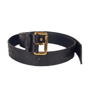Puede incluir: Un cinturón negro con una superficie texturizada que presenta pequeñas hendiduras espaciadas uniformemente. El cinturón incluye una hebilla rectangular de metal dorado y una trabilla de cuero a juego, asegurada con un solo perno.