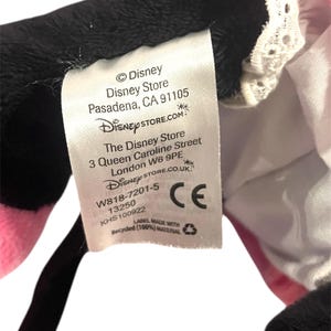 May include: White tag with black text on a black and pink plush toy. The tag reads: &copy;Disney Disney Store Pasadena, CA 91105 DISNEYSTORE.COM The Disney Store 3 Queen Caroline Street London W6 9PE DISNEYSTORE.CO.UK W818-7201-5 13250 KHS100922 CE LABEL MADE WITH Recycled (100%) MATERIAL