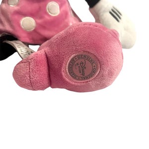 May include: Pink plush Minnie Mouse toy with white polka dots and a black bow. The toy has a white tag on its leg that says "Genuine Disney Store."