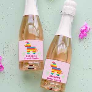 May include: Two champagne bottles with pink labels featuring a colorful piñata design and the text "Stacey's Final Fiesta." Gold and pink party streamers and confetti are scattered around the bottles on a light green background.