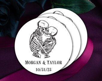 May include: A set of three round white paper coasters with a black and white illustration of two skeletons kissing. The text "MORGAN & TAYLOR 10/31/23" is printed on the bottom coaster.