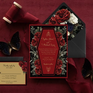 May include: A gothic wedding invitation with a black and red color scheme. The invitation features a coffin-shaped design with red roses and gold lettering. The text on the invitation reads "Lydia Adams and Michael Dean".