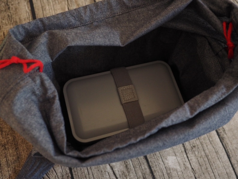 Op de afbeelding: Een grijze lunchtas met een rood trekkoord en een grijze lunchbox erin.