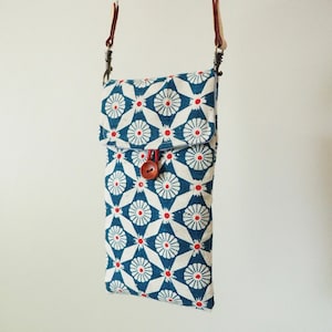 May include: A small blue and white patterned crossbody bag with a red button closure. The bag has a long strap and is made of fabric.