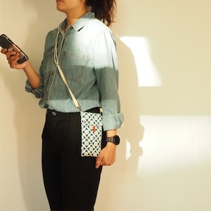 May include: A person wearing a denim shirt and black pants with a white and blue patterned crossbody phone bag.