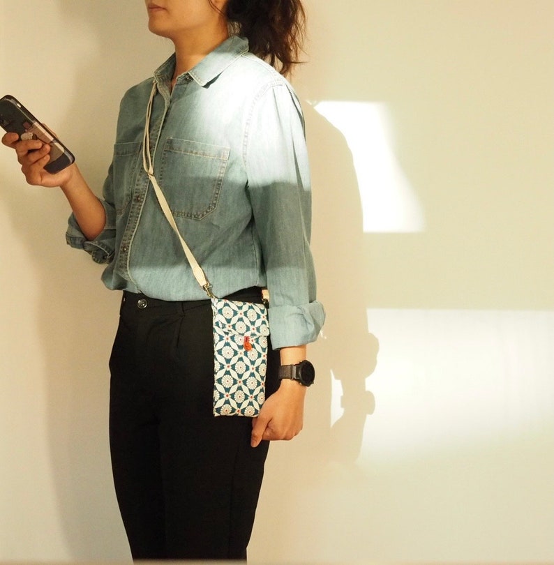 May include: A person wearing a denim shirt and black pants with a white and blue patterned crossbody phone bag.