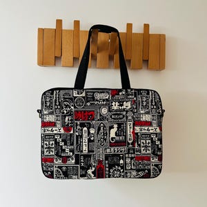 May include: A rectangular laptop bag featuring a black, white, and red collage print of vintage Japanese advertisements and graphic illustrations. The bag has black fabric handles, a zipped closure, and a structured, flat-panel design.