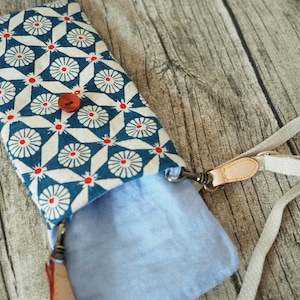 May include: A blue and white patterned fabric phone case with a red button and a beige strap. The case is open and the inside is lined with a light blue fabric.