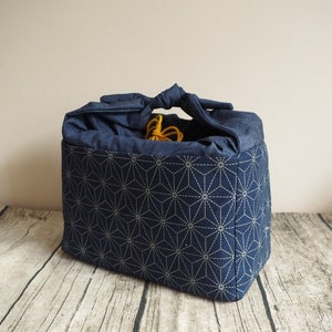 Op de afbeelding: Een blauwe stoffen tas met een wit geometrisch patroon. De tas heeft een geknoopte handvat en is gemaakt van stevig materiaal.