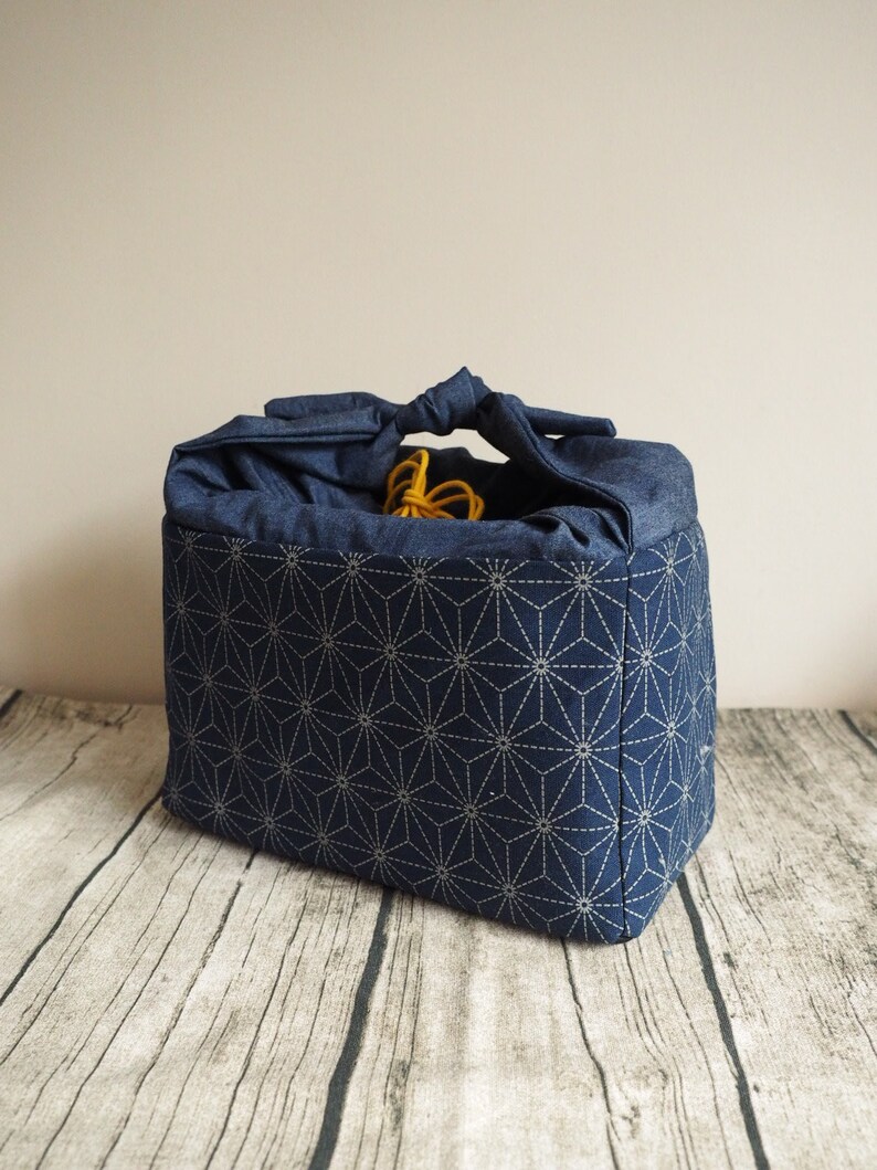 Op de afbeelding: Een blauwe stoffen tas met een wit geometrisch patroon. De tas heeft een geknoopte handvat en is gemaakt van stevig materiaal.