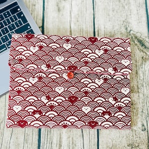May include: A red laptop sleeve with a white and red pattern of stylised cats and waves. The sleeve has a red button closure.