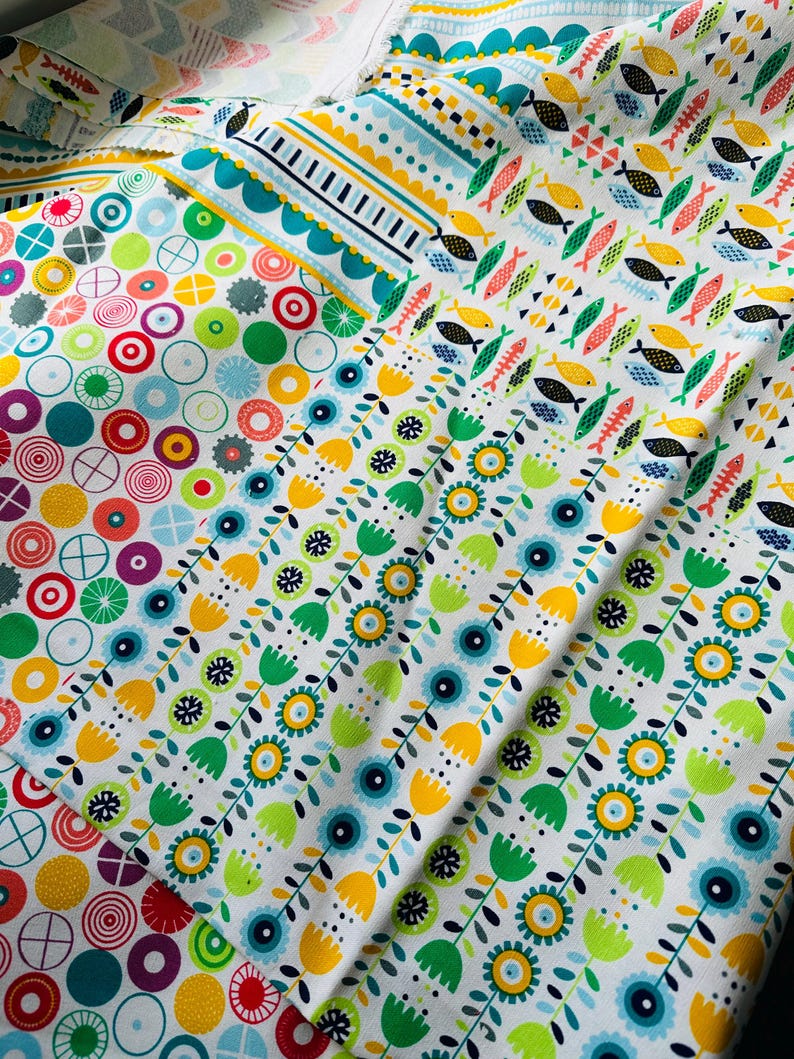May include: A collection of colorful fabric swatches with different patterns. The patterns include circles, flowers, and fish. The fabrics are all white with bright colors.
