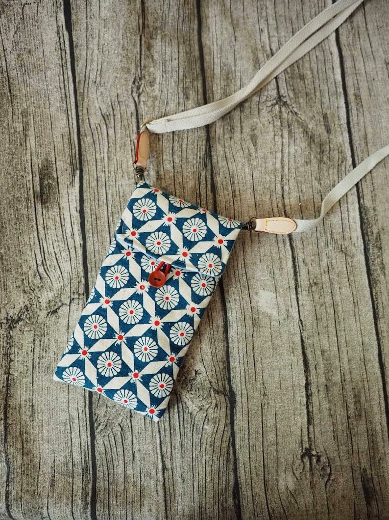 May include: A small blue and white patterned crossbody bag with a red button closure and a long white strap.