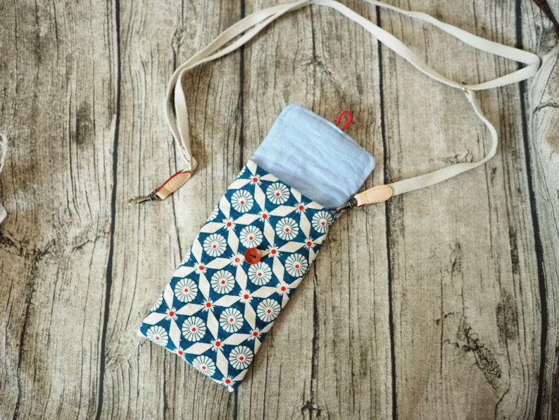 May include: A blue and white patterned fabric pouch with a light blue fabric lining. The pouch is attached to a white strap.