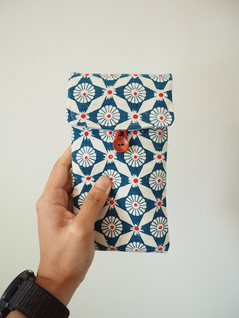 May include: A blue and white fabric pouch with a red and white floral pattern. The pouch has a red button closure.