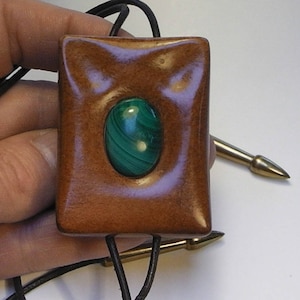 May include: A wooden pendant with a green malachite stone set in the center. The pendant is attached to a black cord.