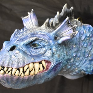 May include: A blue and silver dragon head sculpture with a fierce expression and sharp teeth. The dragon's scales are detailed and textured, and its eyes are painted with a realistic look.