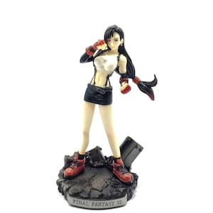 May include: A black-haired female action figure with a white top and black skirt, holding a weapon in each hand. The figure is standing on a rocky base with the words "FINAL FANTASY VII" printed on the front.