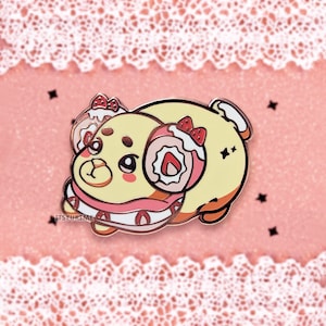 May include: A yellow and pink enamel pin of a cartoon animal wearing a pink and white swirl dessert on its head. The animal has a pink nose and pink cheeks. The pin is on a pink background with white lace.