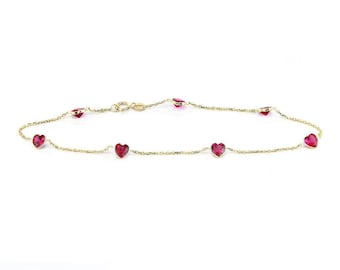 May include: A delicate gold chain anklet with small red heart-shaped gemstones. The anklet has a lobster claw clasp.