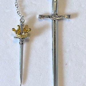 May include: Two silver-toned swords with gold accents. The smaller sword has a crown on the hilt and is attached to the larger sword by a silver chain.